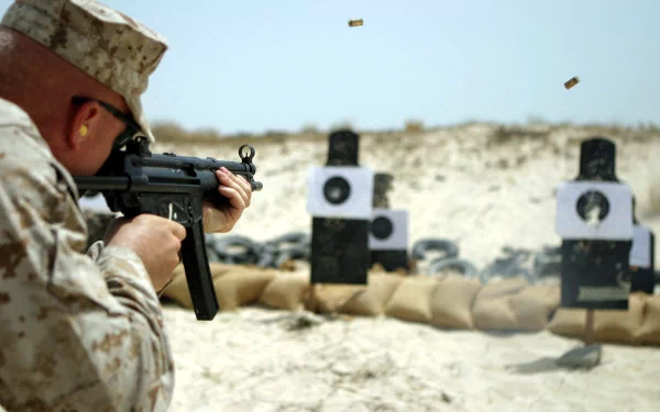 HD desktop wallpaper showing a soldier in military gear aiming a gun at paper targets on a sandy outdoor firing range.