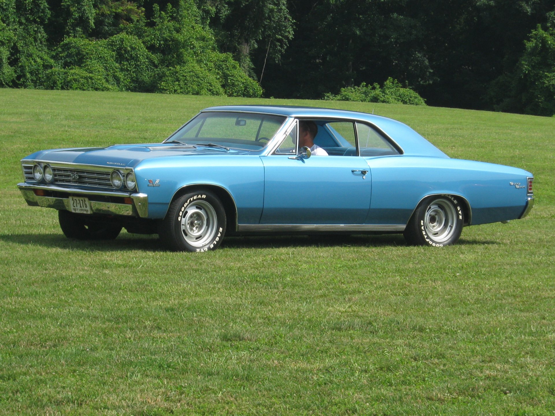 2K Quad HD PC desktop wallpaper featuring a sky-blue Chevrolet classic two-door coupe parked on a green lawn with trees in the background.