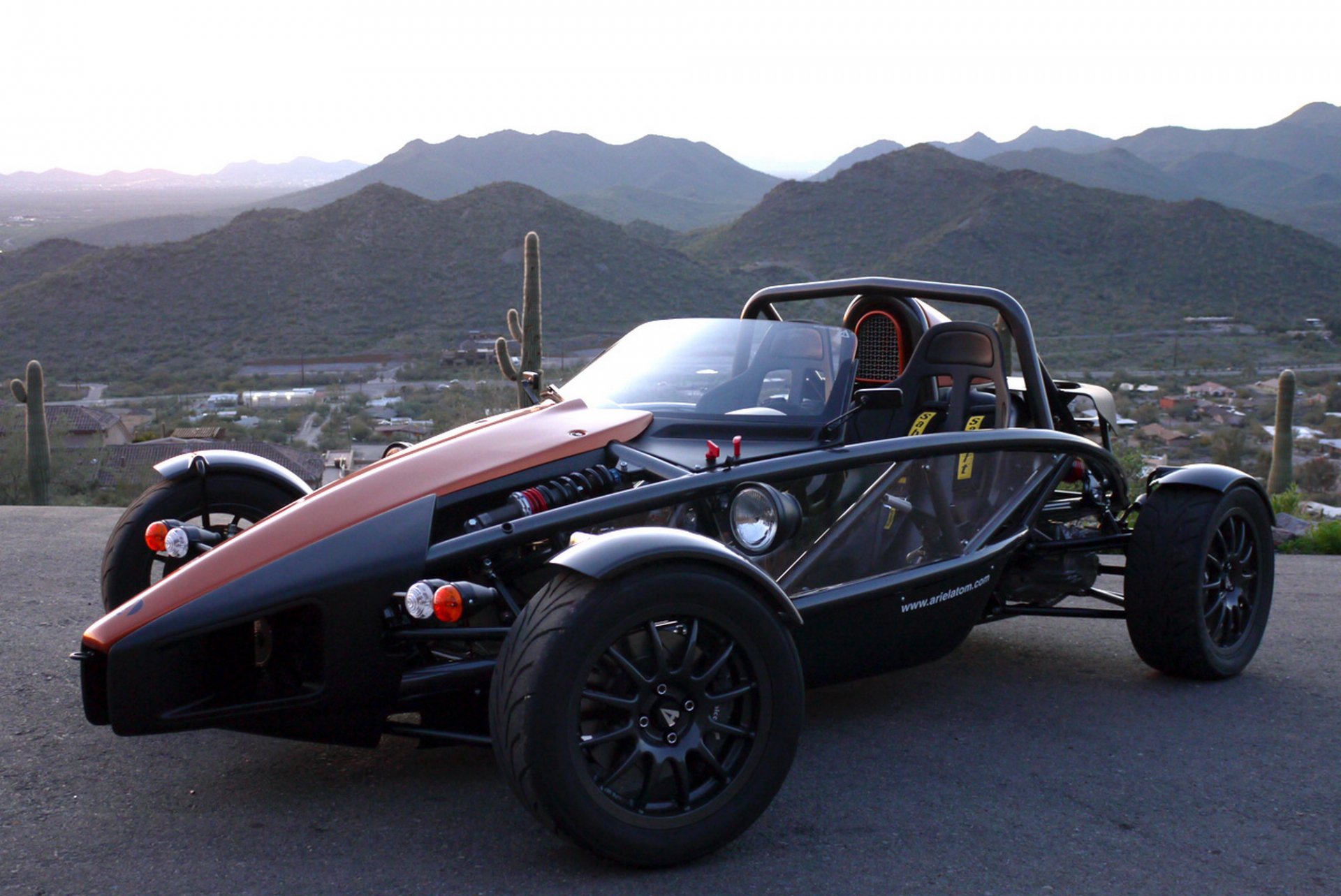 HD desktop wallpaper featuring an Ariel Atom vehicle parked on a road with a mountainous desert landscape in the background.