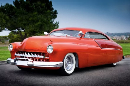 HD PC desktop wallpaper featuring a classic red Mercury vehicle with a sleek, vintage design parked on a road with greenery and distant hills in the background.