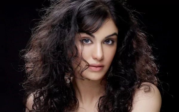 A striking HD desktop wallpaper featuring celebrity Adah Sharma, showcasing her elegant features and voluminous curly hair against a dark background.