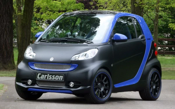 A sleek smart vehicle with a matte black finish and blue accents is parked outdoors, surrounded by lush greenery, serving as an appealing HD desktop wallpaper.