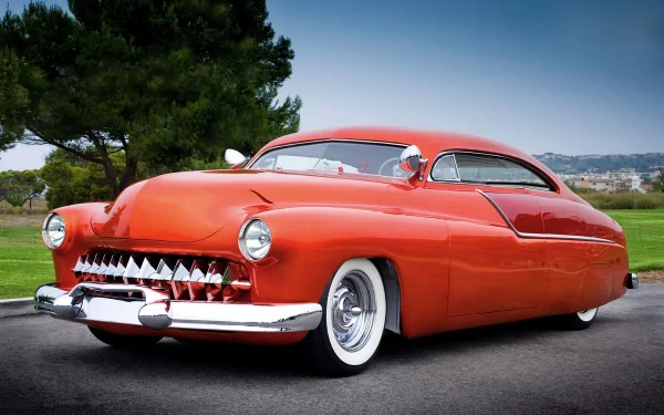 HD PC desktop wallpaper featuring a classic red Mercury vehicle with a sleek, vintage design parked on a road with greenery and distant hills in the background.