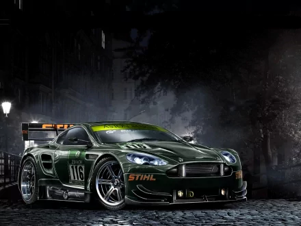HD PC desktop wallpaper featuring a dark green Aston Martin race car with STIHL branding, set against a moody urban night background.