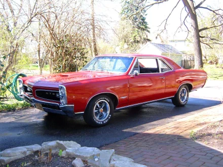 A high-definition desktop wallpaper featuring a red 1966 Pontiac GTO parked on a driveway, surrounded by a scenic outdoor setting.