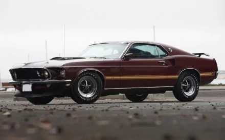 HD PC desktop wallpaper of a maroon Ford Mustang Mach 1 muscle car vehicle, shown in a low front three-quarter view with black stripes and a rear spoiler on wet pavement.