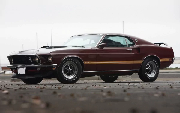 HD PC desktop wallpaper of a maroon Ford Mustang Mach 1 muscle car vehicle, shown in a low front three-quarter view with black stripes and a rear spoiler on wet pavement.