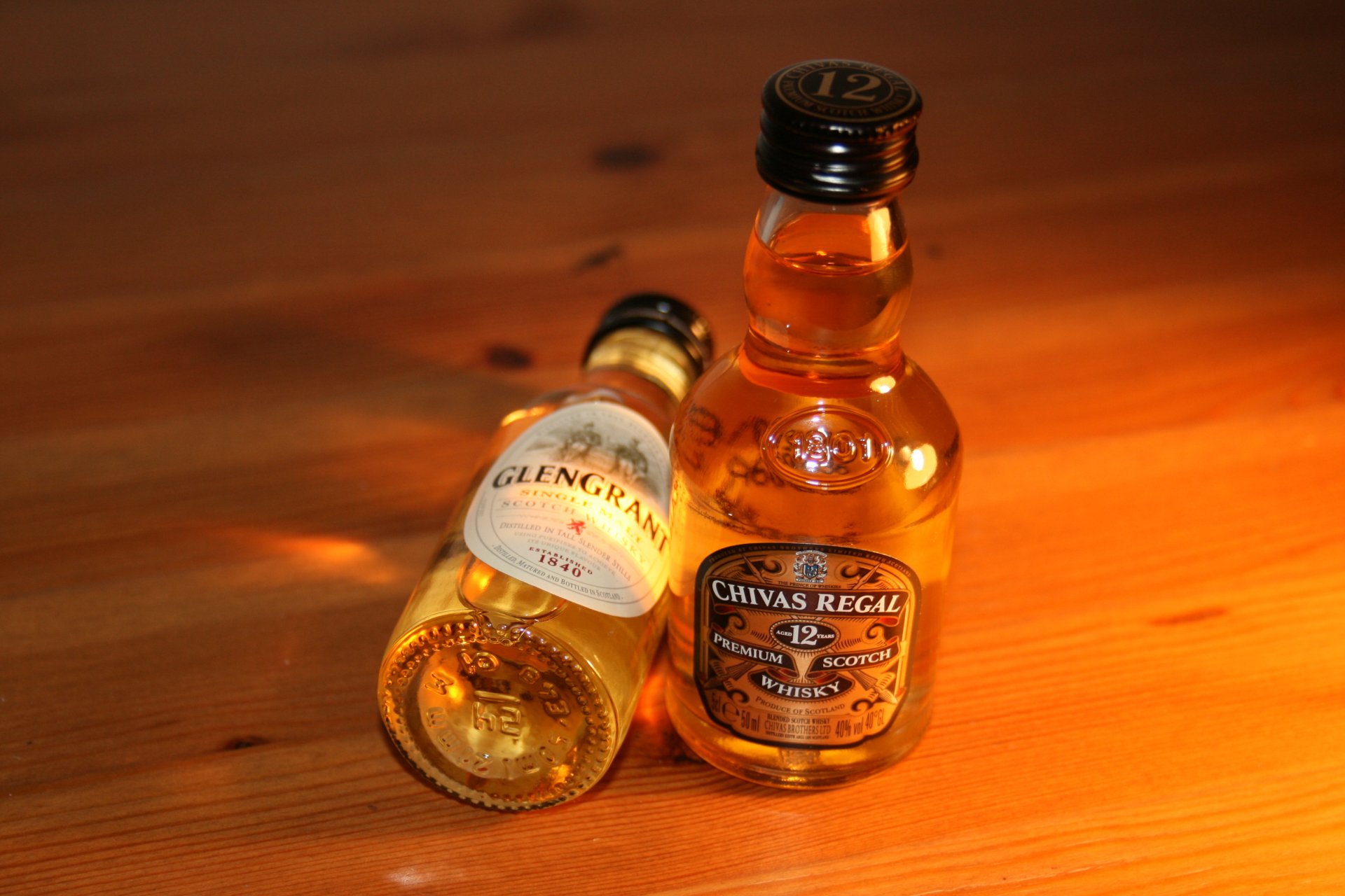 4K Ultra HD wallpaper featuring two small whisky bottles on a wooden surface, illuminated by warm lighting, highlighting rich amber tones and detailed labels.