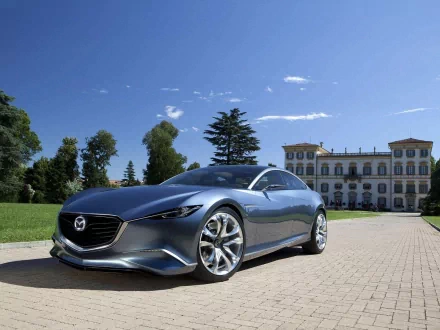 HD PC desktop wallpaper featuring a sleek silver Mazda vehicle parked on a cobblestone driveway with a historic building and clear blue sky in the background.