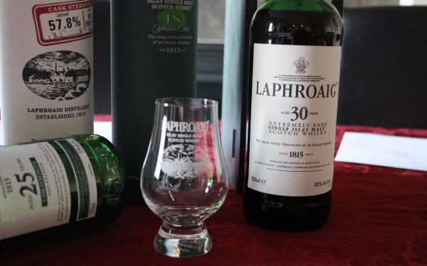A 4K Ultra HD image showcasing Laphroaig Scotch whisky, featuring a bottle of 30-year-old malt and a tasting glass, complemented by other whisky bottles against a rich red backdrop.