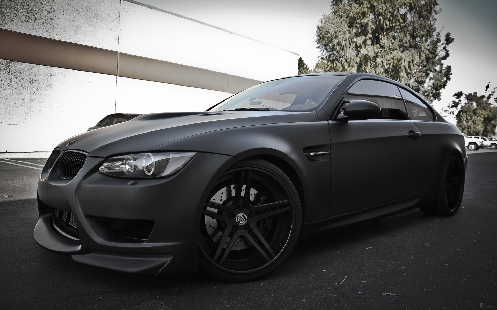 HD PC desktop wallpaper featuring a sleek black BMW vehicle parked outdoors against a minimalist backdrop with trees and a building.