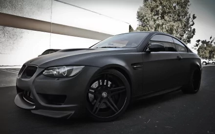 HD PC desktop wallpaper featuring a sleek black BMW vehicle parked outdoors against a minimalist backdrop with trees and a building.