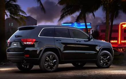 HD desktop wallpaper featuring a sleek black Jeep parked on a street at night, illuminated by colorful neon signs and palm trees in the background.