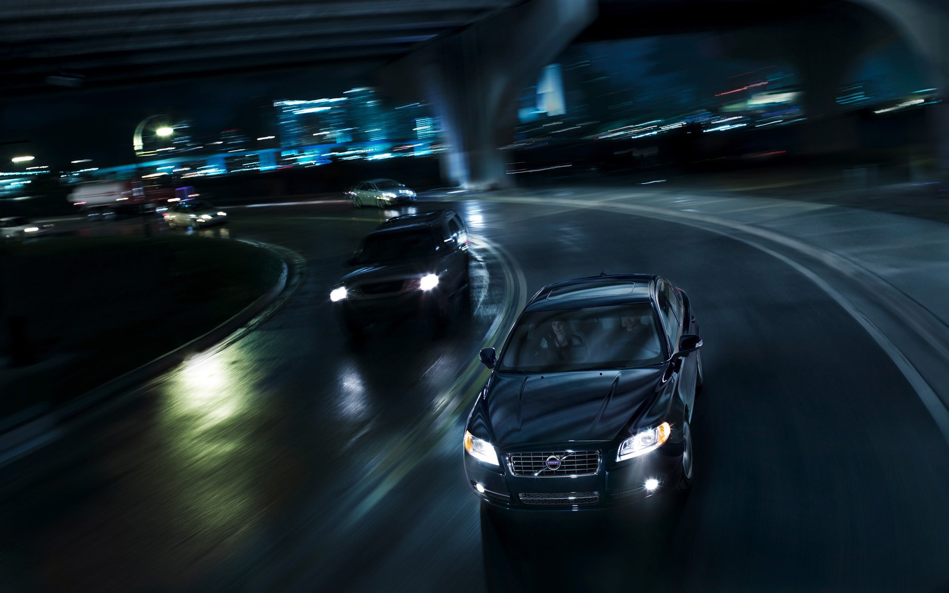 HD PC desktop wallpaper: Volvo vehicle speeding on a wet urban highway at night, motion blur and glowing city lights.