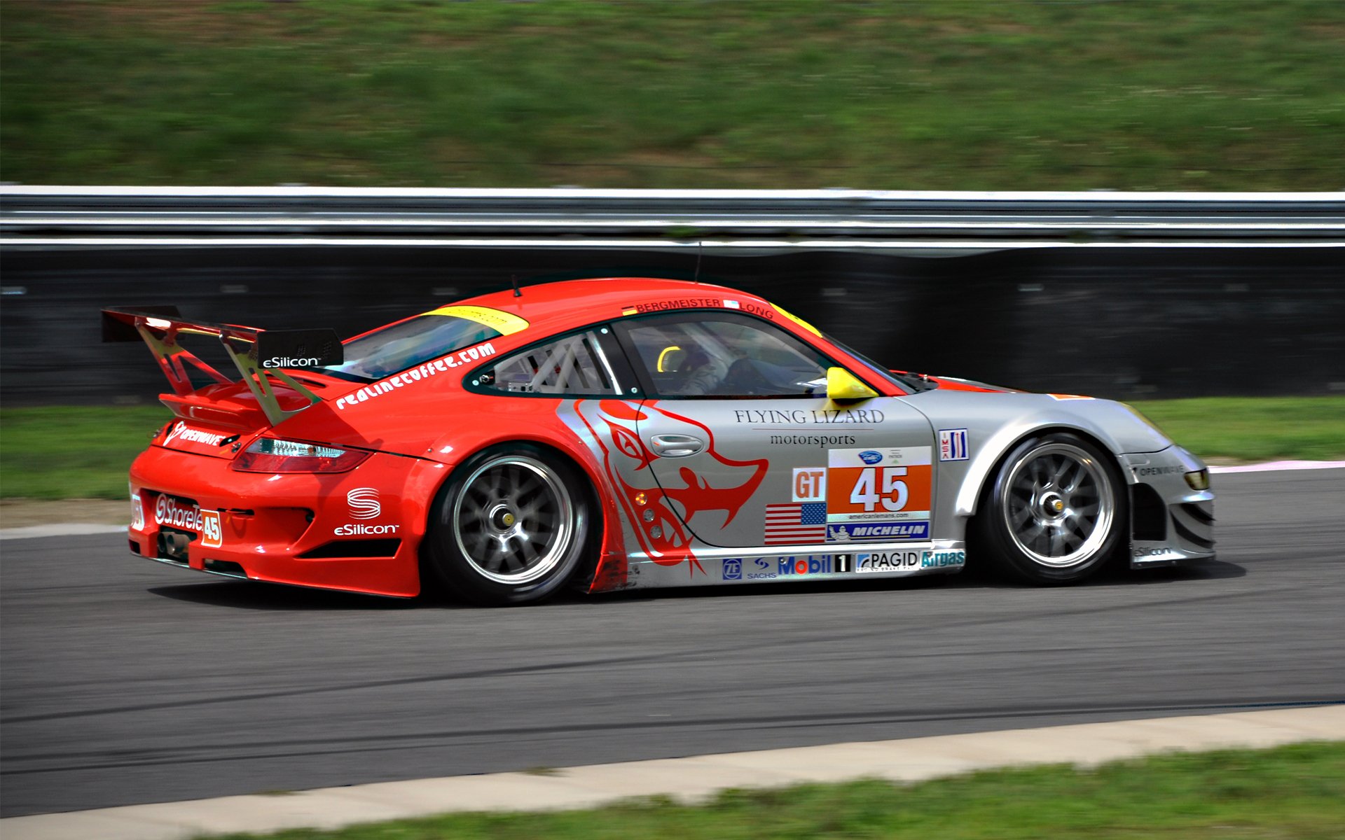 HD PC desktop wallpaper: red-and-silver Porsche race car (#45) tearing along a racetrack, motion-blurred backdrop and grassy runoff.
