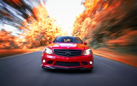 HD desktop wallpaper featuring a red Mercedes vehicle speeding down a road lined with vibrant autumn trees.
