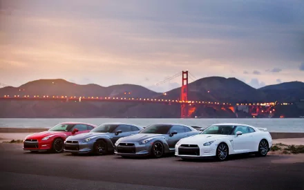HD PC desktop wallpaper showing five Nissan vehicles lined up along a waterfront at sunset with the Golden Gate Bridge and rolling hills in the background.