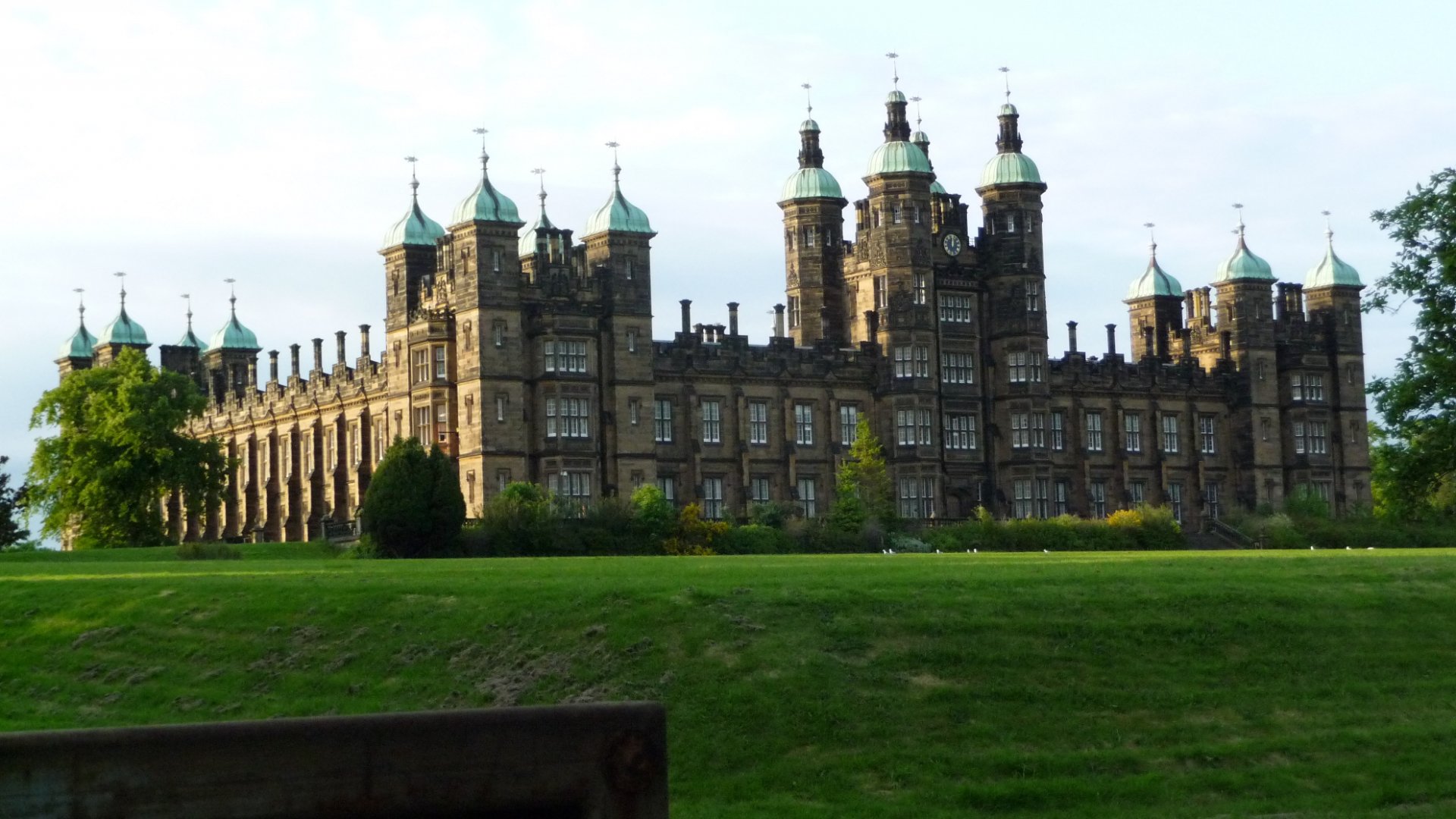 HD PC desktop wallpaper featuring a grand, man-made castle with multiple towers and spires, set against a bright sky and lush green lawn.