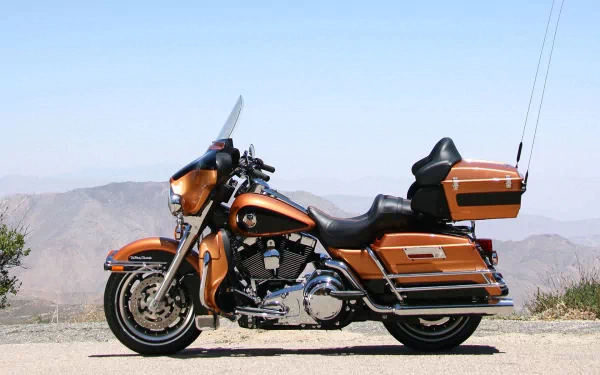 Orange Harley-Davidson Road King touring motorcycle parked on a scenic roadside with distant mountains; HD PC desktop wallpaper.