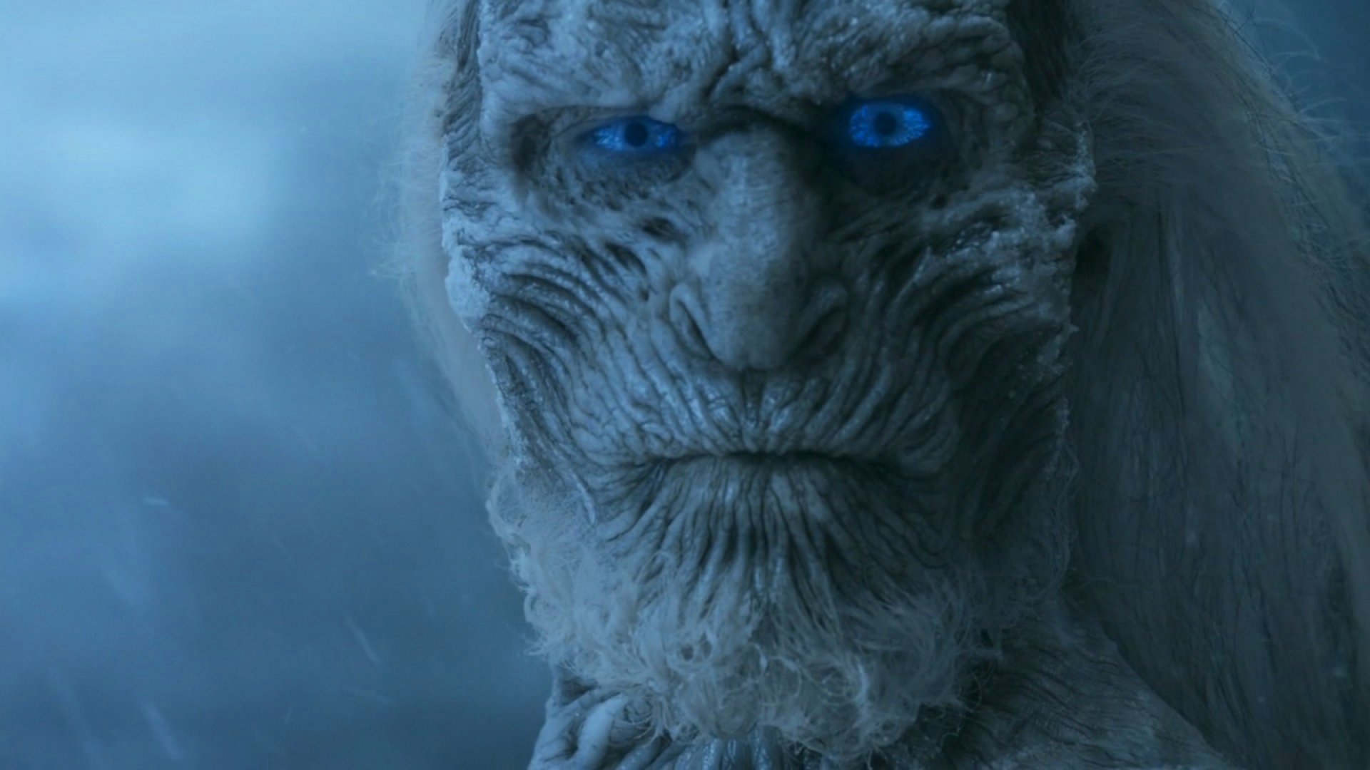 Close-up of a White Walker from the TV show Game of Thrones, featuring icy features and glowing blue eyes, set against a cold, atmospheric background. HD desktop wallpaper.