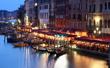 A serene night scene in Venice, showcasing a tranquil canal illuminated by soft lights, with gondolas and vibrant waterfront cafés reflecting on the water's surface.