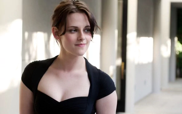 HD desktop wallpaper of American actress Kristen Stewart, looking to the side while standing in a well-lit hallway, wearing a black outfit.