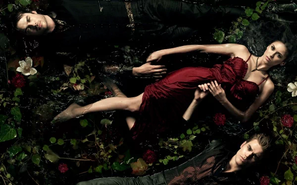 A dramatic HD desktop wallpaper from The Vampire Diaries, featuring three central characters amidst a dark, floral scene, evoking mystery and intrigue in the series.