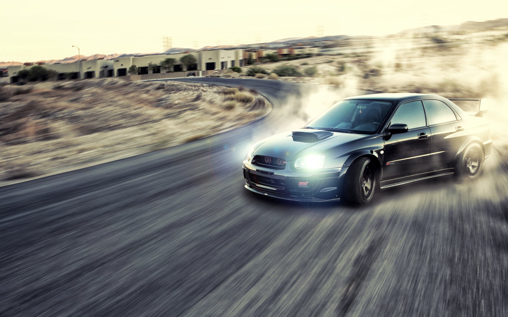 HD PC desktop wallpaper featuring a black Subaru drifting sharply on a winding road, kicking up smoke and dust in a dynamic motion scene.