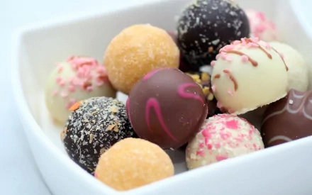 HD PC desktop wallpaper featuring a close-up of assorted colorful sweet truffles in a white bowl, highlighting rich textures and delicate toppings.