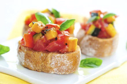 Close-up HD desktop wallpaper featuring fresh bruschetta topped with diced tomatoes, yellow bell peppers, and basil leaves on crusty bread slices.