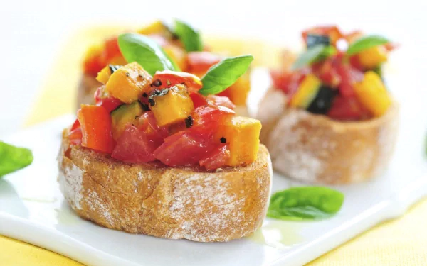 Close-up HD desktop wallpaper featuring fresh bruschetta topped with diced tomatoes, yellow bell peppers, and basil leaves on crusty bread slices.