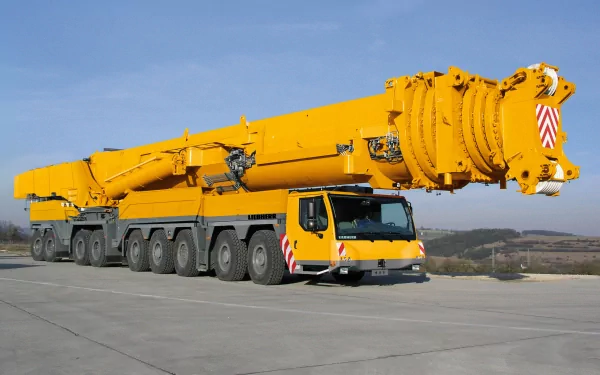 HD desktop wallpaper featuring a bright yellow Liebherr construction crane vehicle against a clear blue sky on an open concrete surface.