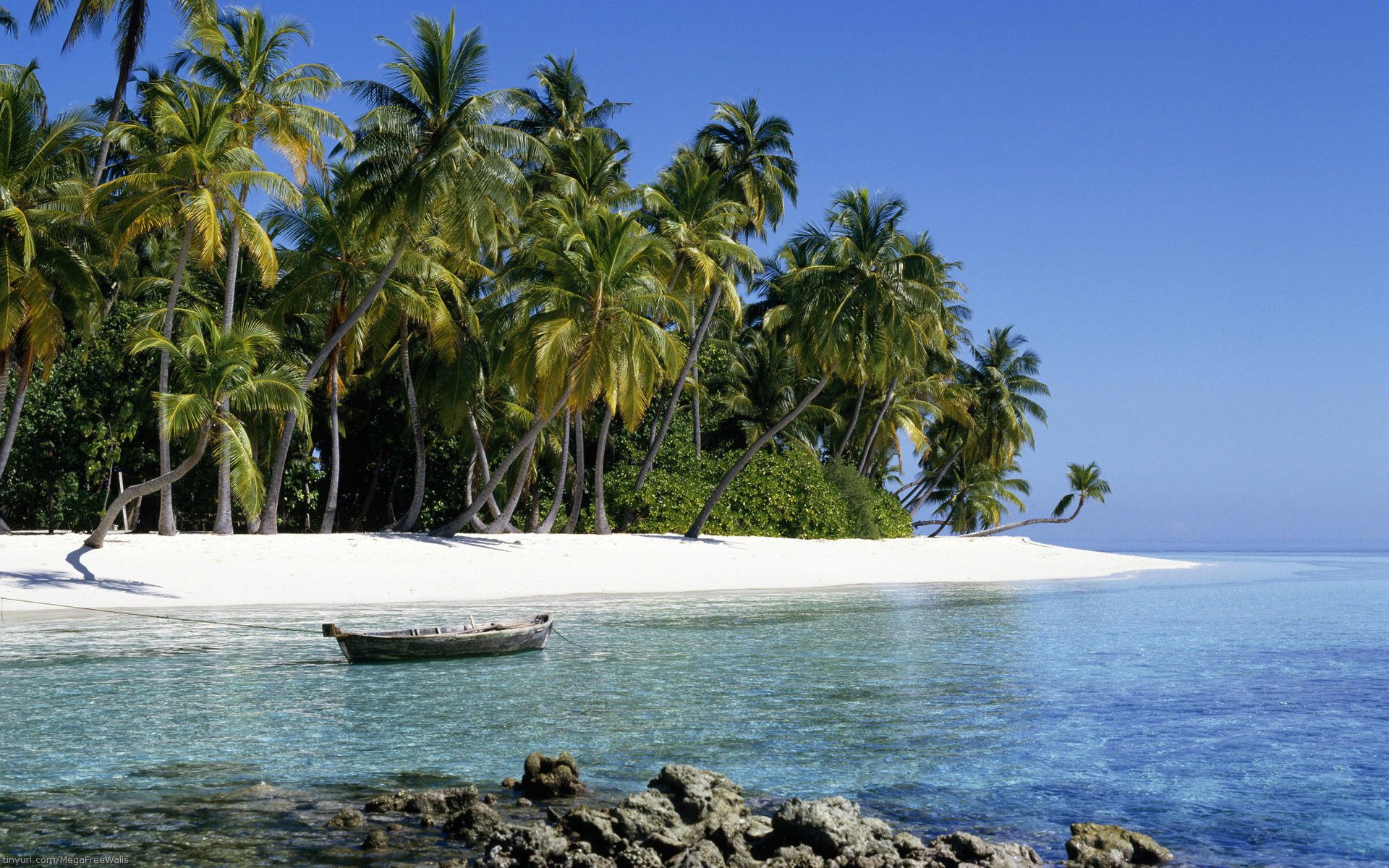 HD PC desktop wallpaper: photographic tropical beach with palm trees, white sand, clear turquoise ocean and a small boat moored near the shore.