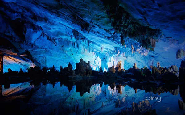 Blue-lit interior of Reed Flute Cave with natural rock formations and clear reflections on the water, showcasing a stunning nature scene as an HD PC desktop wallpaper.