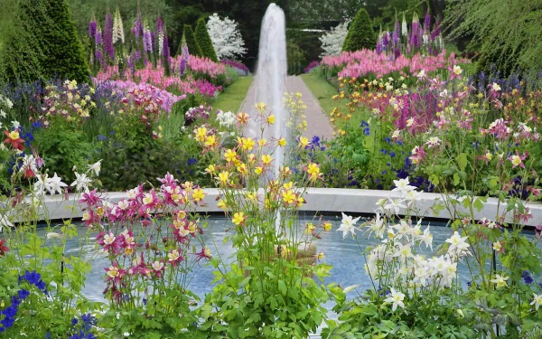 A vibrant garden with colorful flowers surrounds a man-made fountain, captured in high-definition as a desktop wallpaper and background.