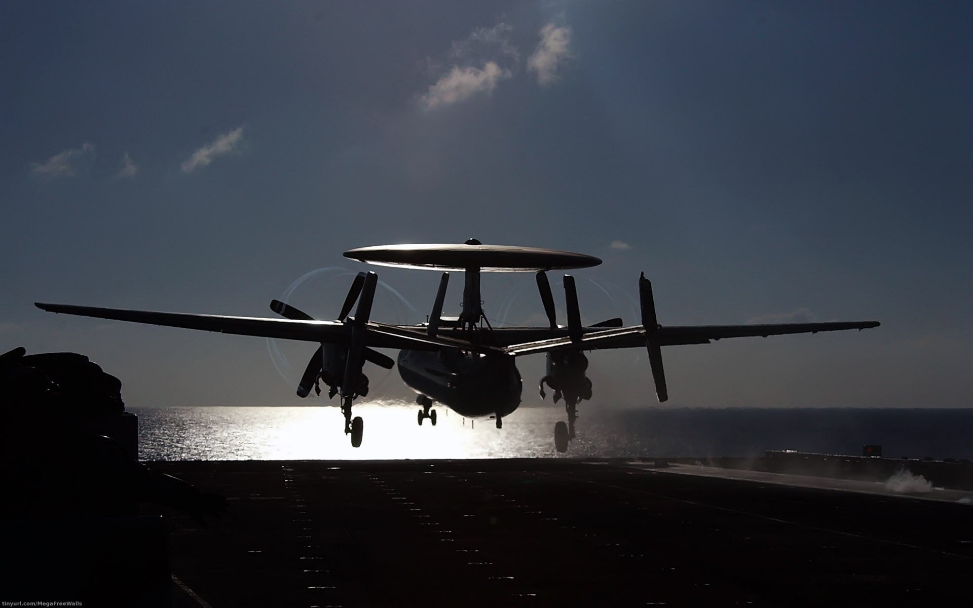 Silhouetted Northrop Grumman E-2 Hawkeye military aircraft landing at dusk, captured in an HD desktop wallpaper background.