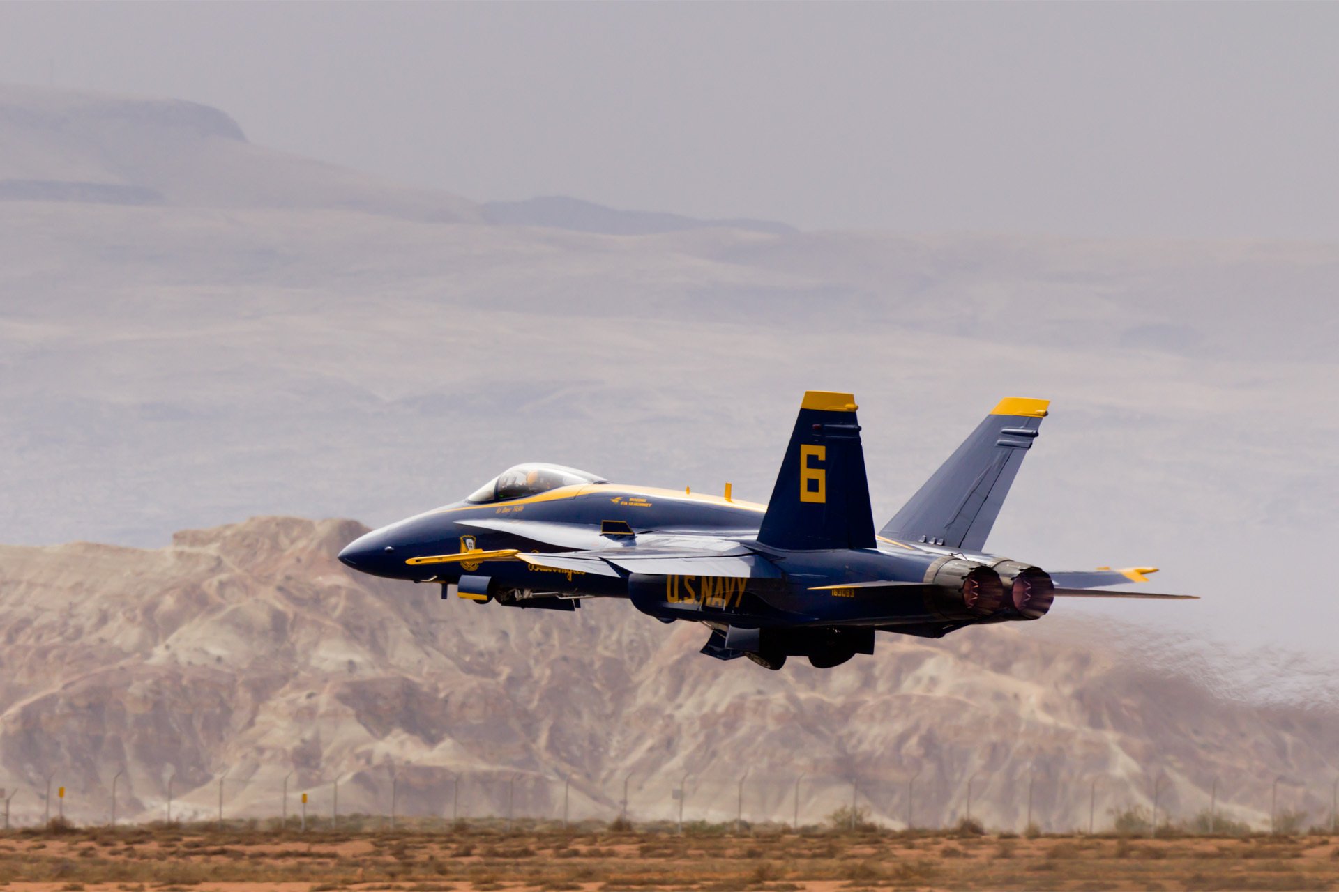 HD PC desktop wallpaper background: blue-and-yellow military fighter jet numbered 6 making a low pass over a desert landscape at an air show.