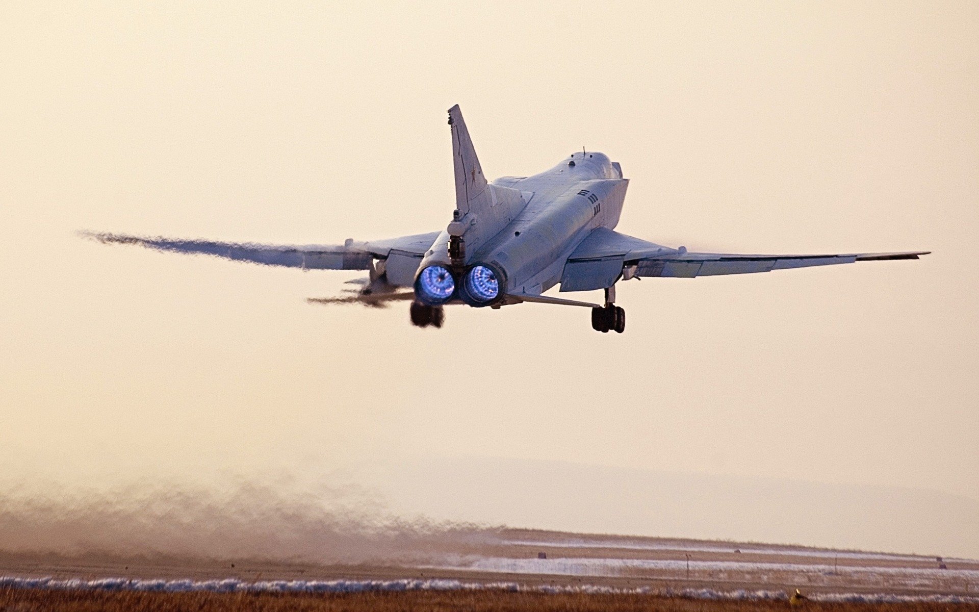 Rear view of a Tupolev Tu-22 military bomber lifting off over a coastal runway at sunset — HD PC desktop wallpaper background.