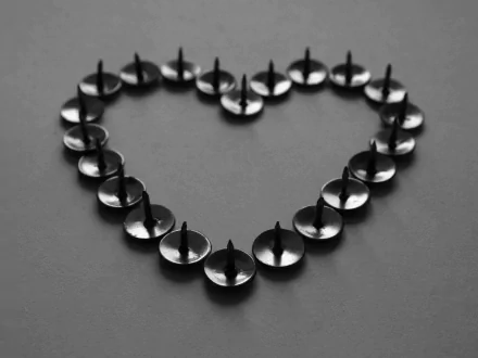 An artistic HD desktop wallpaper featuring a heart shape formed by black thumbtacks against a dark background, symbolizing love.