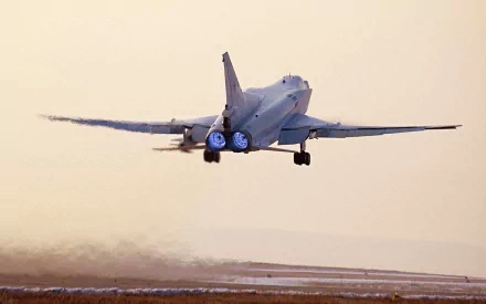 Rear view of a Tupolev Tu-22 military bomber lifting off over a coastal runway at sunset — HD PC desktop wallpaper background.