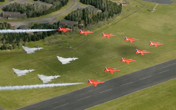 Aerial view of Red Arrows jet fighters and Eurofighter Typhoons flying in formation over a runway during an air show, showcasing military precision and skill.