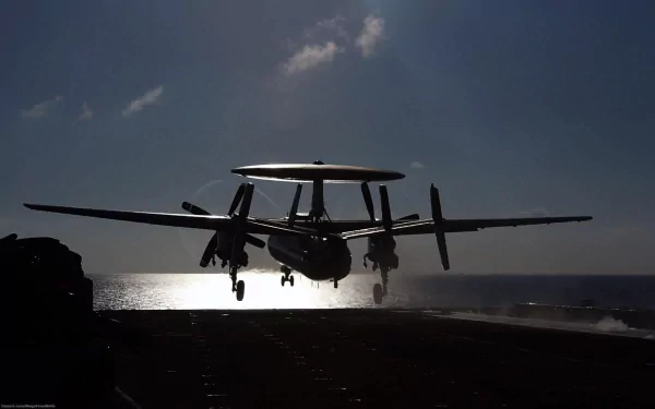 Silhouetted Northrop Grumman E-2 Hawkeye military aircraft landing at dusk, captured in an HD desktop wallpaper background.