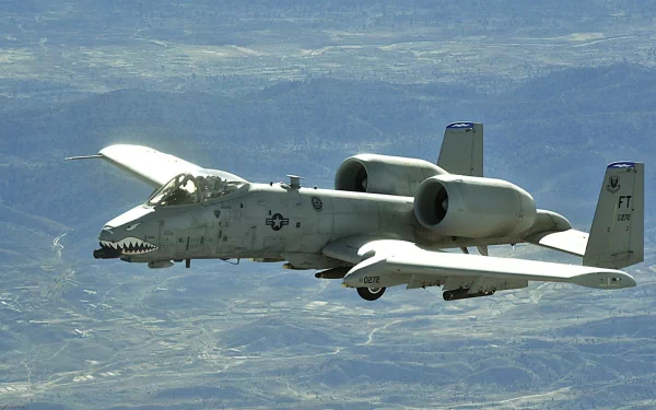 A Fairchild Republic A-10 Thunderbolt II military airplane soars over a rugged landscape, showcasing its iconic design. This HD image serves as an impressive desktop wallpaper.