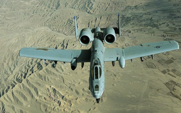 Aerial view of a Fairchild Republic A-10 Thunderbolt II aircraft flying over a rugged landscape, showcasing its military design and capabilities in this HD desktop wallpaper.