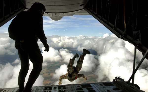 A paratrooper in military gear jumps from an aircraft, silhouetted against a backdrop of clouds, capturing the intensity and bravery of soldiers in action. HD desktop wallpaper.