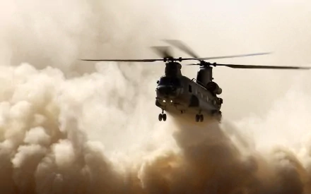 Military Boeing CH-47 Chinook helicopter kicking up a cloud of dust as it hovers toward the viewer, rotor blur against a sandy sky — 2K Quad HD PC desktop wallpaper
