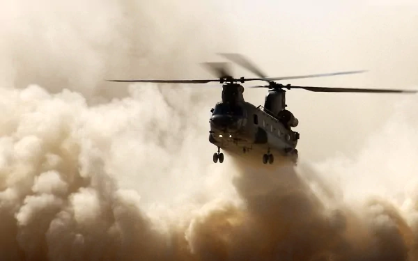Military Boeing CH-47 Chinook helicopter kicking up a cloud of dust as it hovers toward the viewer, rotor blur against a sandy sky — 2K Quad HD PC desktop wallpaper
