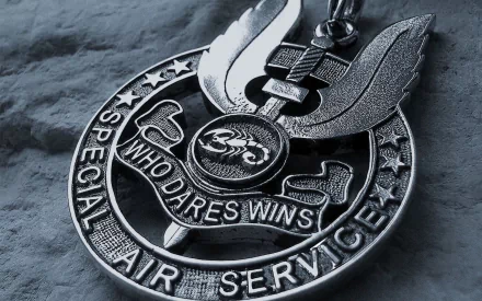 HD desktop wallpaper featuring a close-up of a Special Air Service military medal with the motto Who Dares Wins on a textured background.