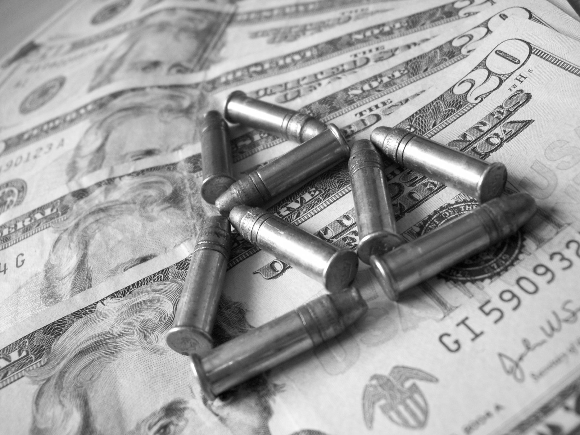 HD desktop wallpaper showing a close-up of metallic bullets arranged on US dollar bills, highlighting man-made objects with a monochrome, high-detail finish.
