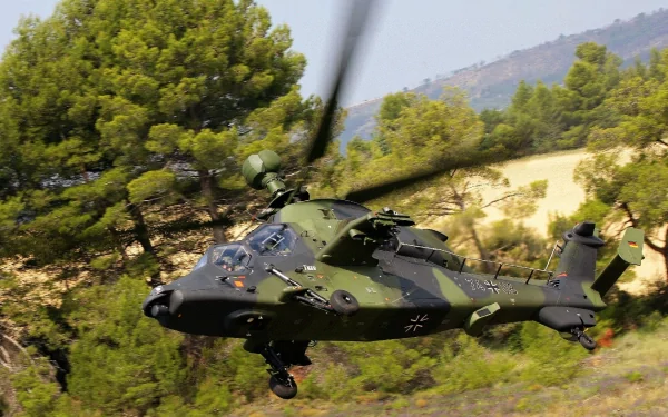 HD desktop wallpaper of a Eurocopter Tiger attack helicopter flying low over a forested landscape, showcasing its military design and camouflage.